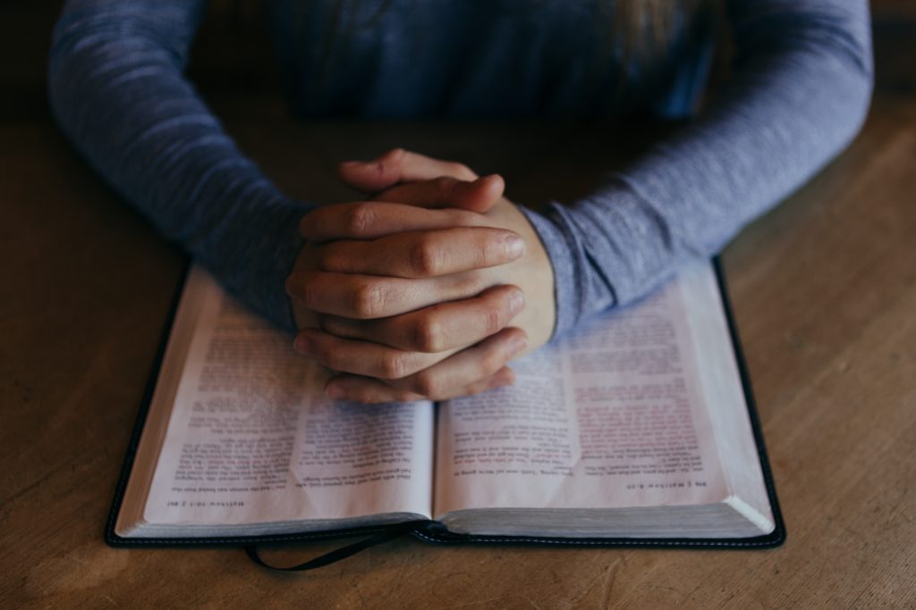 A man's hands clasped and resting on an open Bible