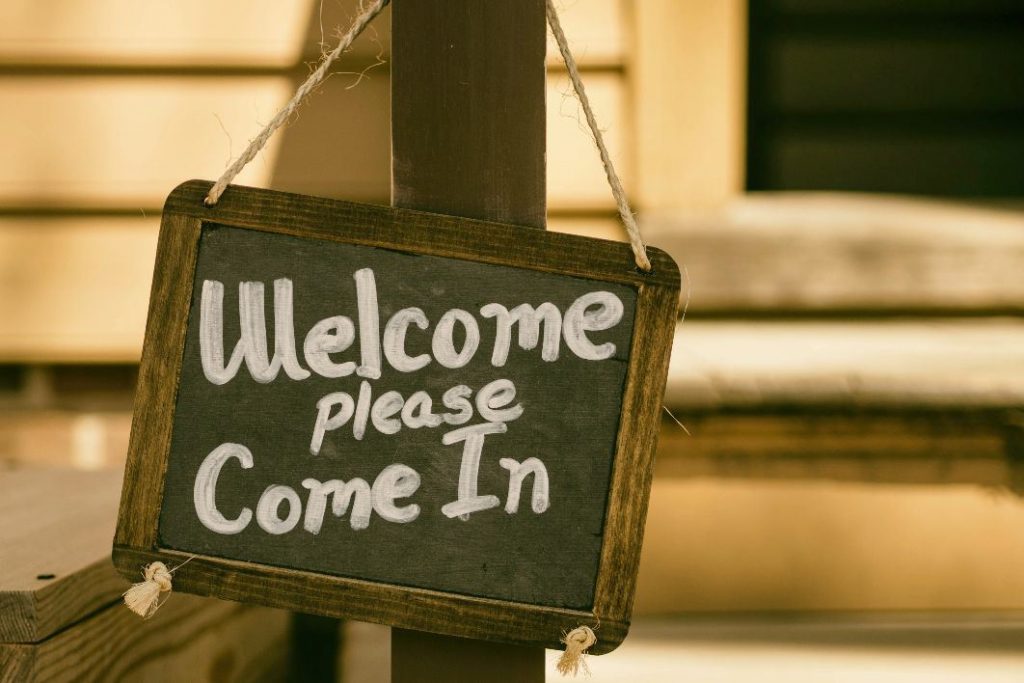 Chalk board hanging on post with the words "Welcome please come in"